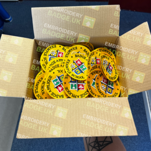 reduce overstock of school badges by ordering appliqué school badges from embroidery badge uk a hand holding a box of school embroidered badges which can be easily appliquéd on to school blazers